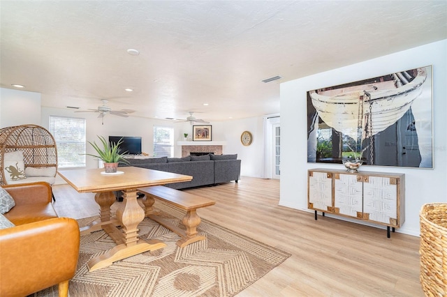 dining space with visible vents, a fireplace, light wood-style flooring, and ceiling fan