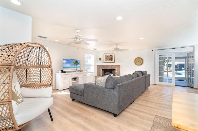 living area with visible vents, a ceiling fan, a tile fireplace, light wood-style flooring, and recessed lighting