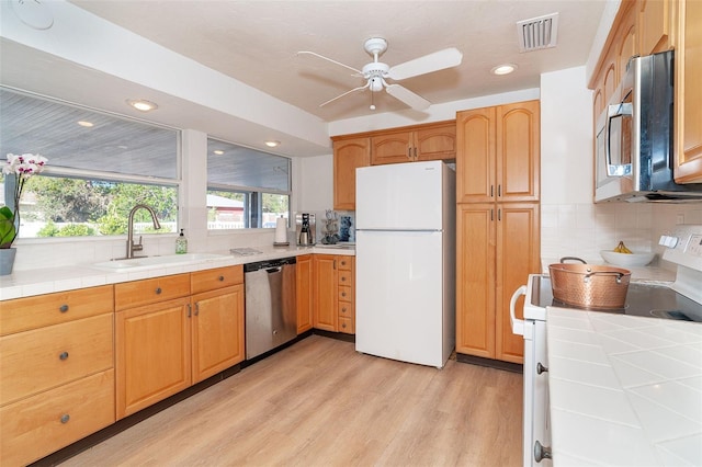 kitchen with a sink, visible vents, appliances with stainless steel finishes, light wood-type flooring, and tile counters