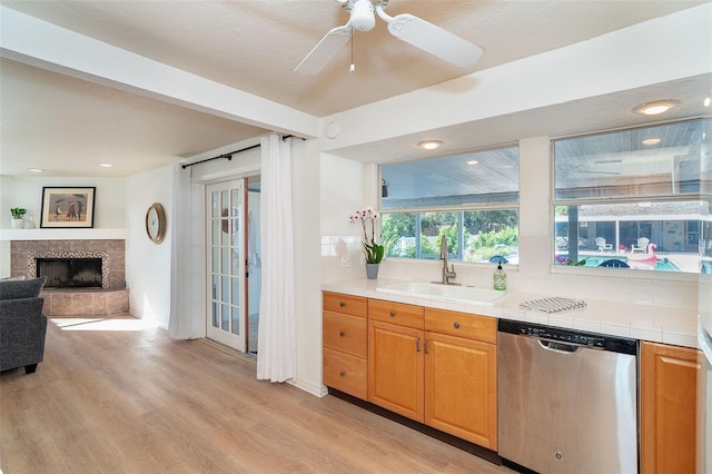 kitchen with tile counters, light wood-style flooring, stainless steel dishwasher, open floor plan, and a sink