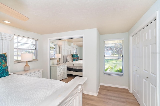 bedroom featuring baseboards, light wood-style flooring, a textured ceiling, two closets, and recessed lighting