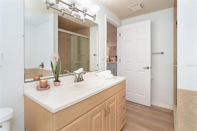 bathroom with toilet, wood finished floors, vanity, visible vents, and a stall shower