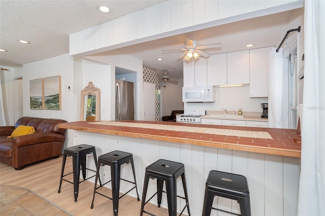 kitchen with white microwave, stainless steel fridge, a kitchen bar, and white cabinets