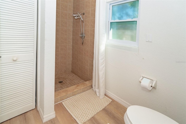 bathroom with a closet, toilet, a shower stall, wood finished floors, and baseboards