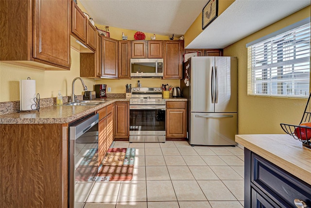 kitchen with appliances with stainless steel finishes, a textured ceiling, vaulted ceiling, sink, and light tile patterned flooring