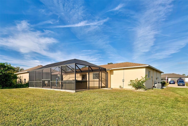 back of house with central AC, glass enclosure, a hot tub, and a lawn