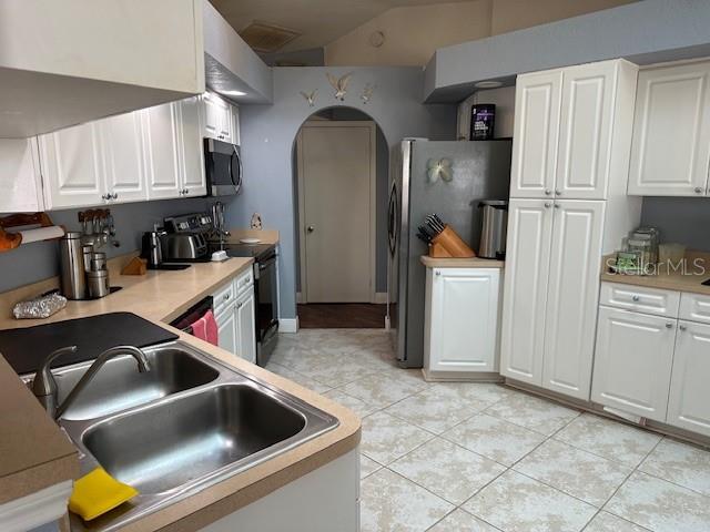 kitchen featuring white cabinetry, sink, stainless steel appliances, lofted ceiling, and light tile patterned flooring