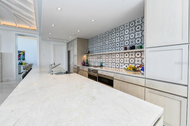 kitchen with backsplash, sink, light stone counters, and oven