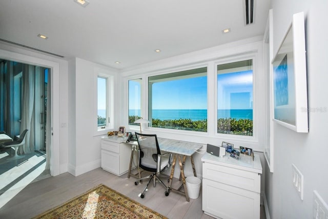 home office featuring built in desk, light hardwood / wood-style floors, and a water view