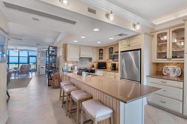 kitchen with a kitchen breakfast bar, sink, an island with sink, cream cabinetry, and stainless steel appliances