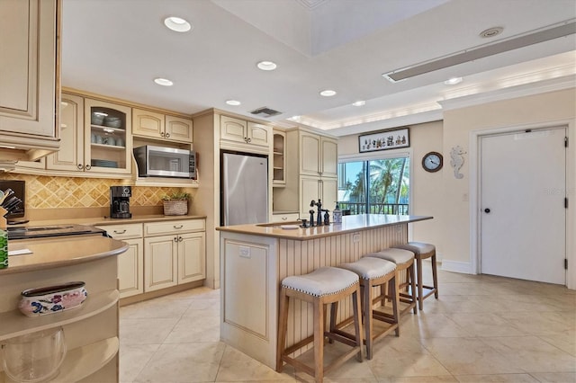 kitchen featuring backsplash, a center island with sink, sink, a tray ceiling, and stainless steel appliances
