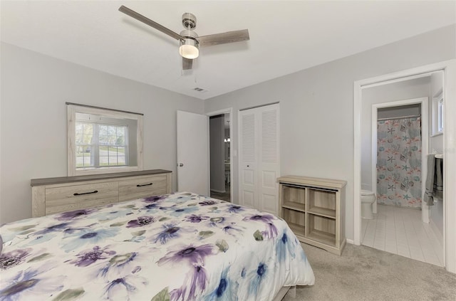 bedroom featuring ceiling fan, a closet, light colored carpet, and ensuite bath