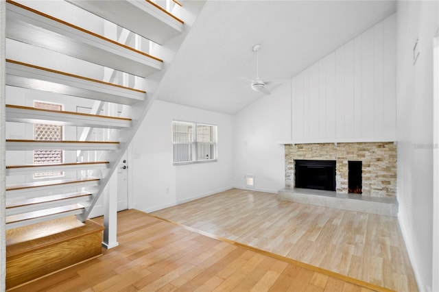 unfurnished living room with ceiling fan, a stone fireplace, high vaulted ceiling, and light hardwood / wood-style flooring