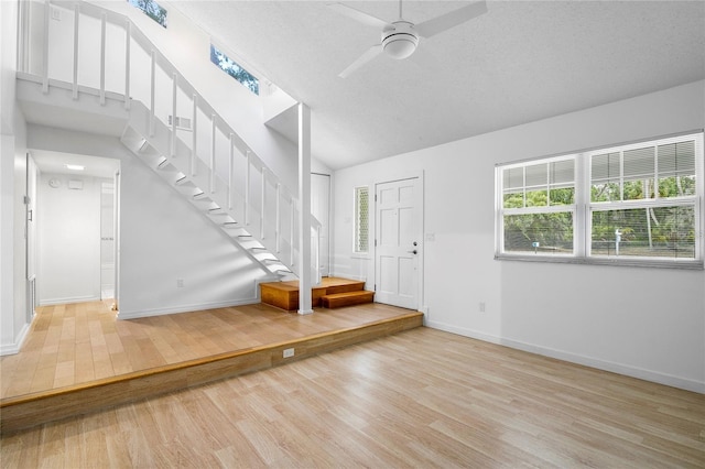 entryway with a textured ceiling, ceiling fan, light hardwood / wood-style floors, and lofted ceiling