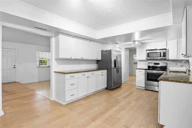 kitchen featuring stainless steel appliances, sink, light hardwood / wood-style flooring, dark stone countertops, and white cabinetry