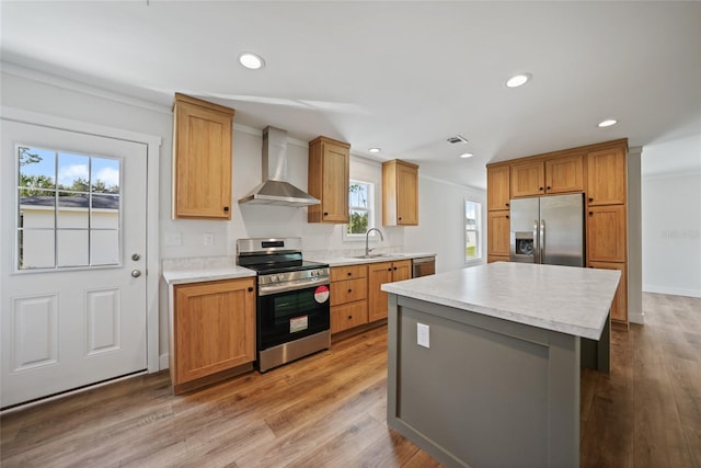 kitchen with sink, a center island, wall chimney range hood, appliances with stainless steel finishes, and light wood-type flooring