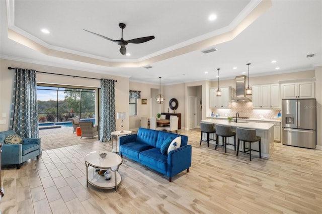 living room with a raised ceiling, ceiling fan, crown molding, and light wood-type flooring