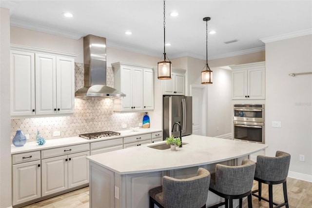 kitchen with pendant lighting, a kitchen island with sink, sink, wall chimney exhaust hood, and stainless steel appliances