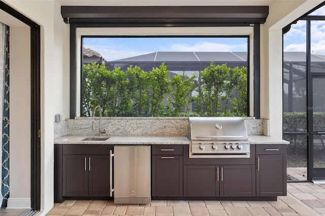 view of patio / terrace featuring glass enclosure, a grill, sink, and an outdoor kitchen