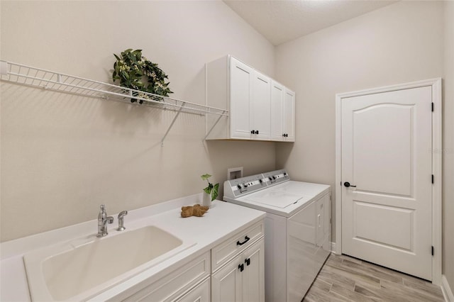 clothes washing area featuring washer and clothes dryer, sink, cabinets, and light hardwood / wood-style floors