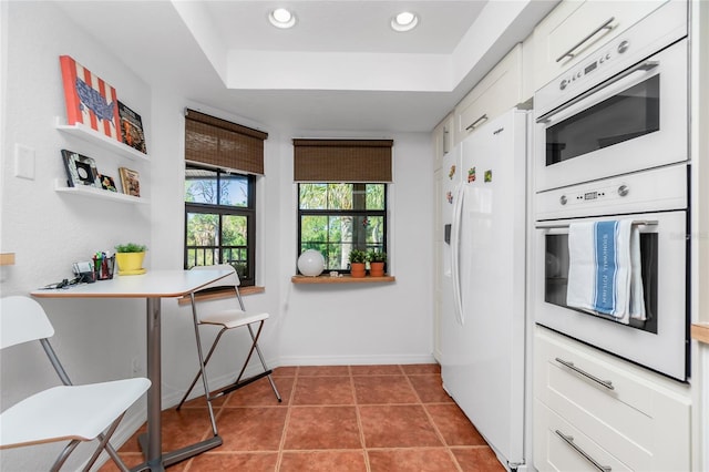 kitchen with white cabinets, tile patterned flooring, white fridge with ice dispenser, and a tray ceiling