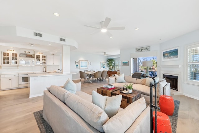 living area featuring ceiling fan, visible vents, light wood-style floors, and a fireplace with raised hearth