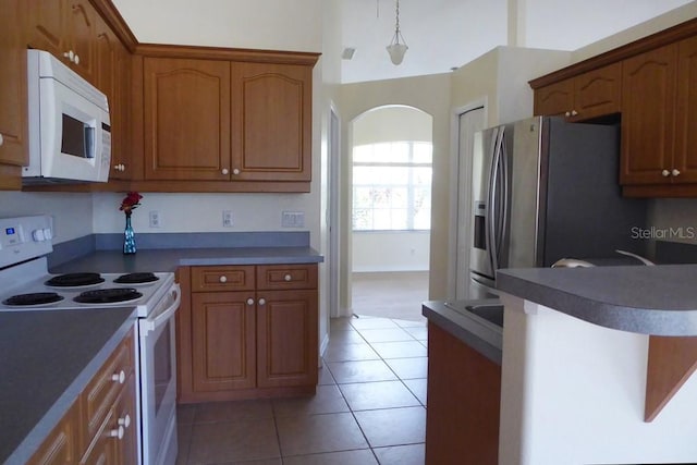 328 Baytree Dr, Rotonda West, FL 33947 - kitchen featuring white appliances, light tile patterned floors, brown cabinetry, and arched walkways