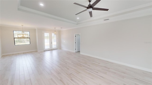 spare room featuring french doors, crown molding, light wood-type flooring, a raised ceiling, and ceiling fan with notable chandelier