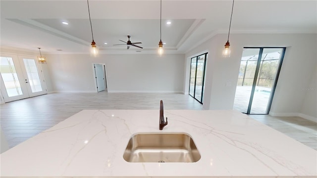 kitchen featuring french doors, sink, light stone counters, hanging light fixtures, and a raised ceiling