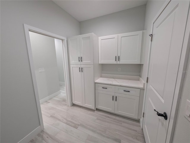 interior space with white cabinetry, light stone counters, and light hardwood / wood-style flooring