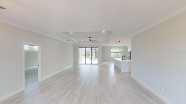 unfurnished living room with ornamental molding, a raised ceiling, sink, and light wood-type flooring