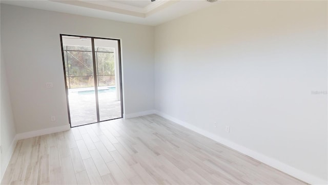 empty room with a tray ceiling and light hardwood / wood-style floors