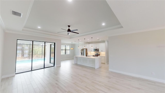 unfurnished living room with ornamental molding, ceiling fan, light wood-type flooring, and a tray ceiling