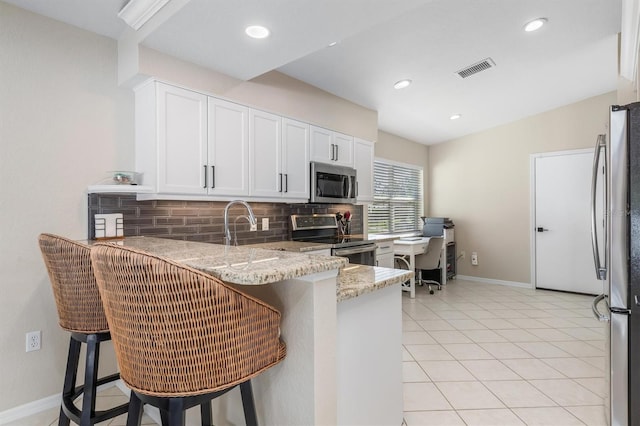 kitchen with kitchen peninsula, appliances with stainless steel finishes, white cabinets, and a breakfast bar area