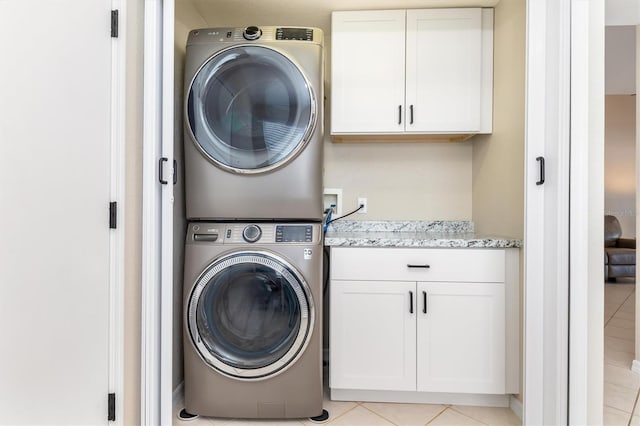 laundry room featuring cabinets, stacked washing maching and dryer, and light tile patterned floors