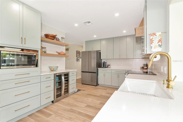 kitchen with appliances with stainless steel finishes, light wood-type flooring, backsplash, beverage cooler, and sink