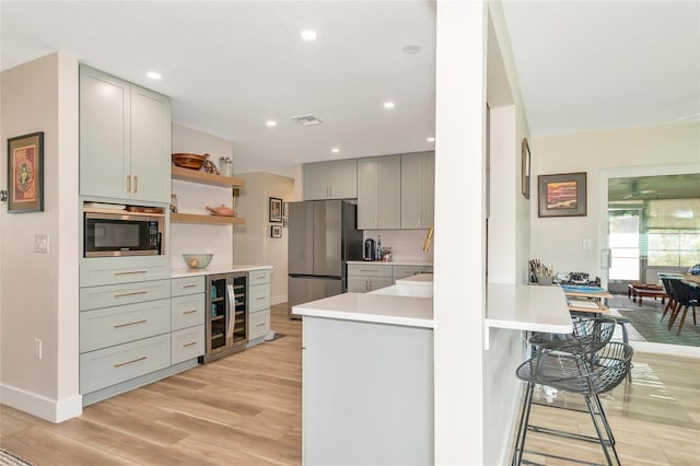 kitchen featuring a kitchen breakfast bar, light hardwood / wood-style flooring, appliances with stainless steel finishes, kitchen peninsula, and beverage cooler