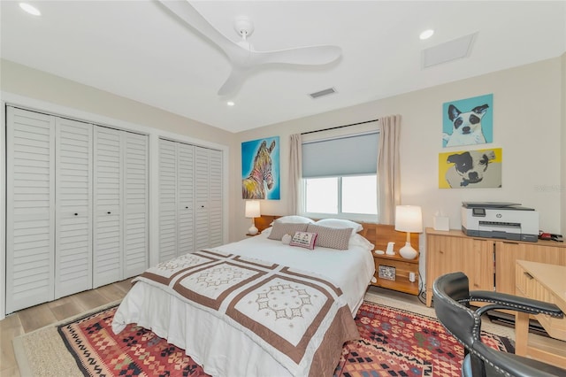 bedroom with ceiling fan, multiple closets, and light hardwood / wood-style flooring