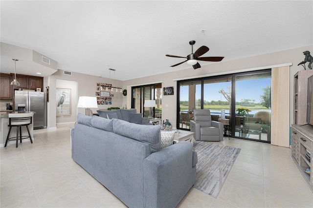 living room featuring a textured ceiling, ceiling fan, a water view, and light tile patterned floors