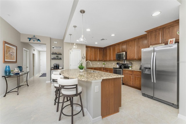 kitchen with a kitchen island with sink, sink, a breakfast bar area, light stone countertops, and stainless steel appliances