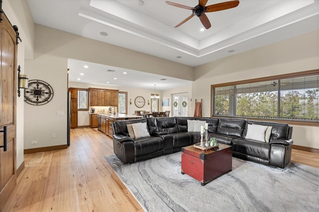 living room with a barn door, light hardwood / wood-style floors, a raised ceiling, and ceiling fan