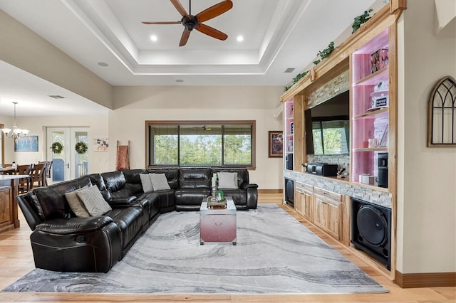 living room with ceiling fan with notable chandelier, light wood-type flooring, and a tray ceiling