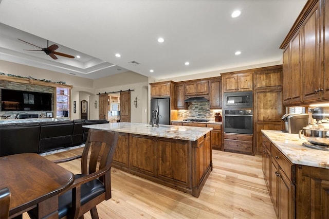 kitchen featuring a kitchen island with sink, a barn door, light stone countertops, tasteful backsplash, and stainless steel appliances