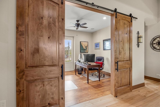 home office with ceiling fan, a barn door, and light hardwood / wood-style floors