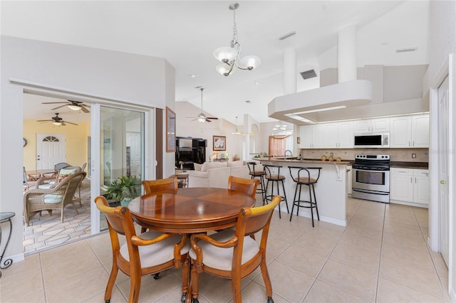 dining space with ceiling fan with notable chandelier, high vaulted ceiling, and light tile patterned flooring