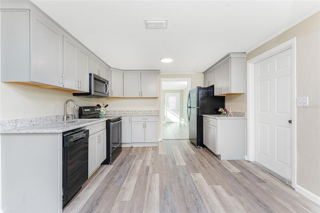 kitchen with black appliances, sink, gray cabinets, light hardwood / wood-style floors, and light stone counters