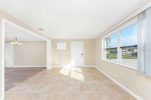 tiled empty room featuring an inviting chandelier