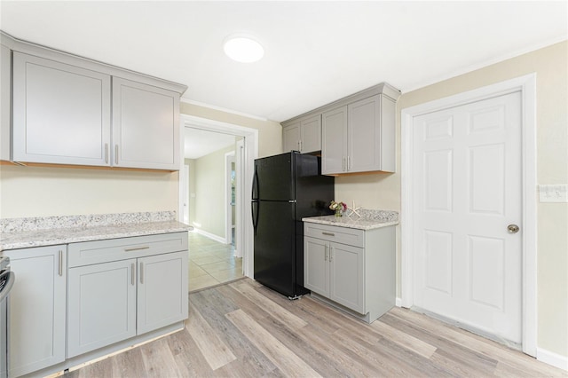 kitchen featuring gray cabinets, stove, light stone counters, black fridge, and light wood-type flooring