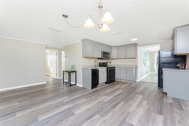 kitchen with gray cabinets, an inviting chandelier, hanging light fixtures, black appliances, and light wood-type flooring