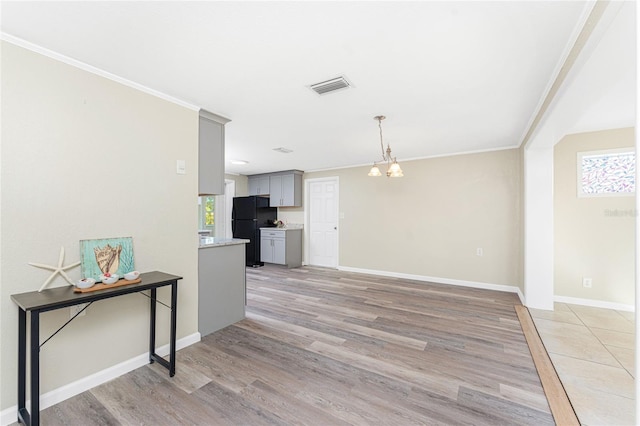 interior space with crown molding, an inviting chandelier, light hardwood / wood-style flooring, black refrigerator, and gray cabinets